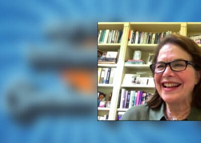 SherryLansing A woman in glasses is smiling in front of a book shelf.