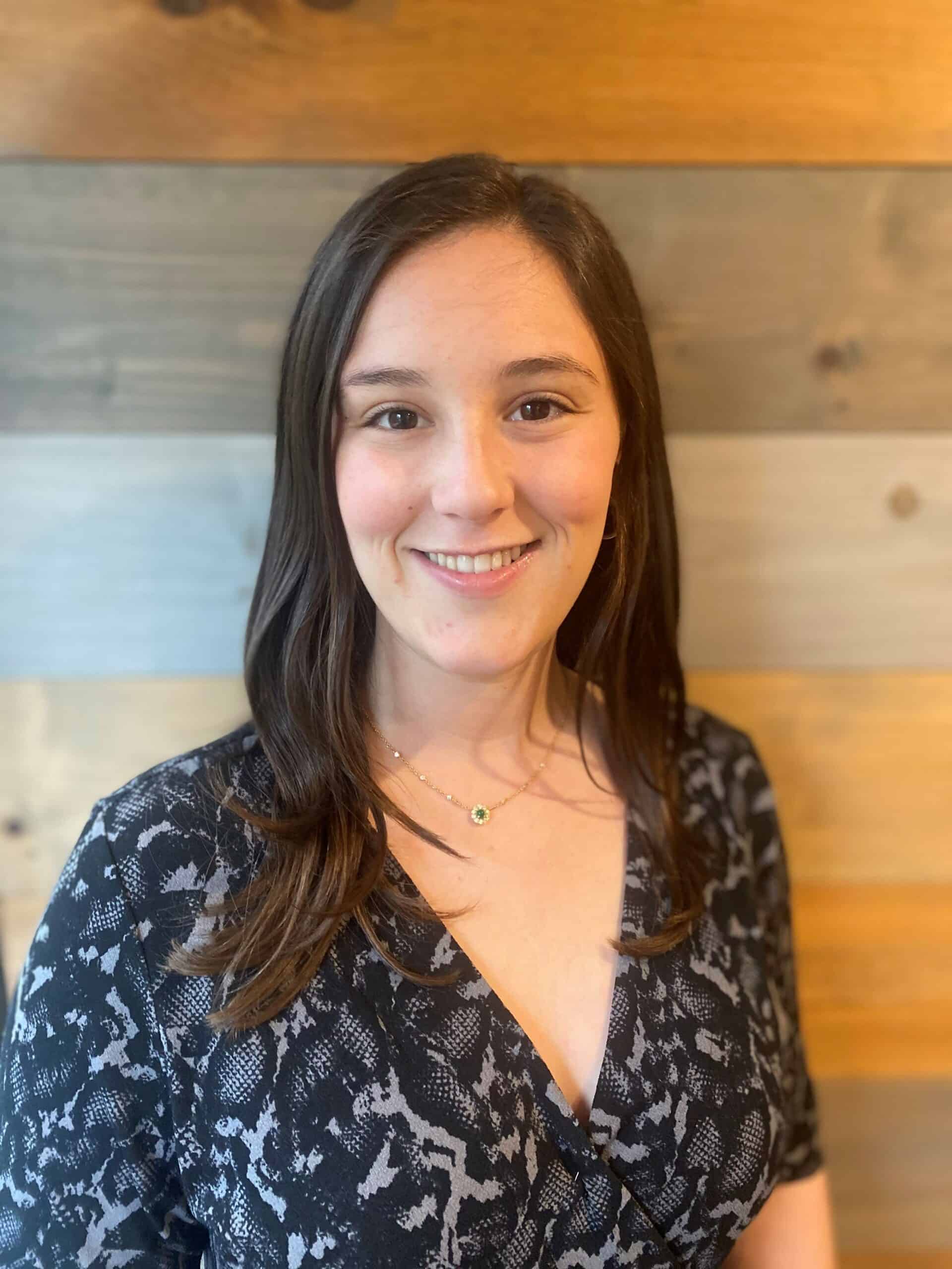Carly Headshot A woman smiling in front of a wooden wall.