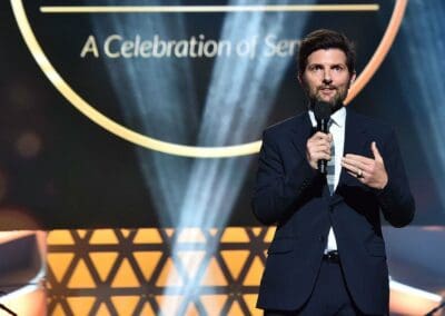 289741650_580346573653417_5513808350992842318_n A man in a suit speaking into a microphone.
