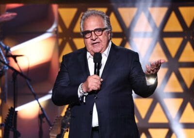jim gianopulos mptf100 A man in a suit and glasses is holding a microphone.