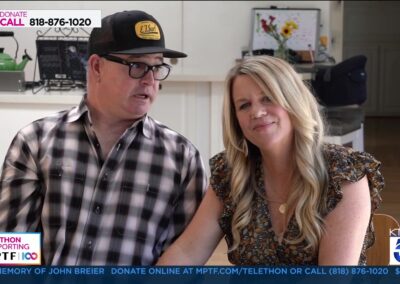 vlcsnap-2024-03-15-10h54m25s813 A man wearing a black and yellow cap sits next to a woman with long blonde hair; both appear on a telethon broadcast with informational text and donation numbers displayed on the screen.