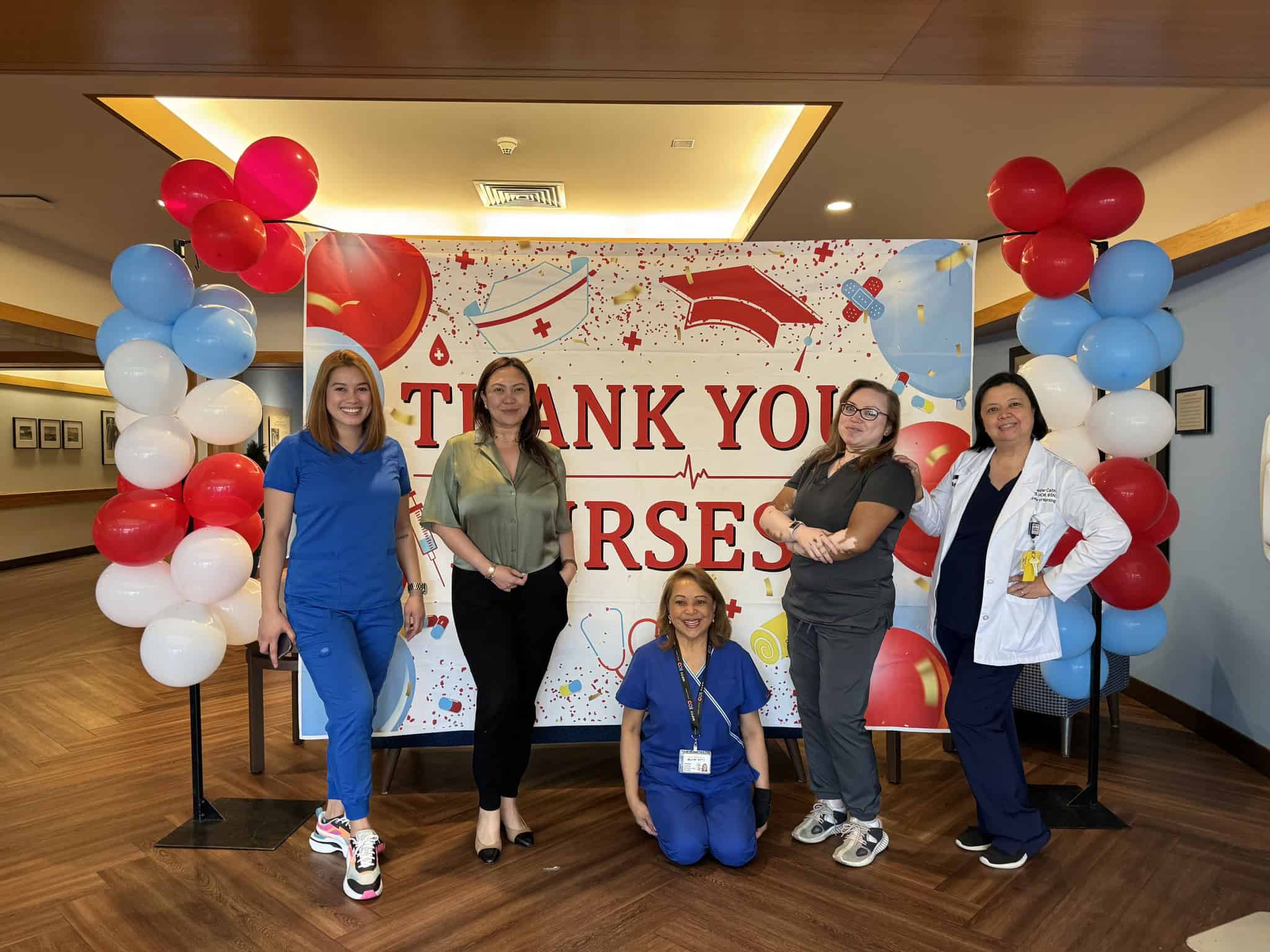 442435169_998745475146856_2670790435510543401_n Five healthcare professionals are standing in front of a "Thank You Nurses" banner decorated with balloons. Four are standing and one is kneeling, all smiling.