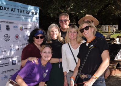 DATR 23166_508 A group of people smiling at a daytime outdoor event, standing in front of a sign with sponsors' logos.
